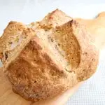 a loaf of Irish Brown Bread set in a wooden cutting board with a green checkered background