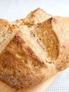 a loaf of Irish Brown Bread set in a wooden cutting board with a green checkered background
