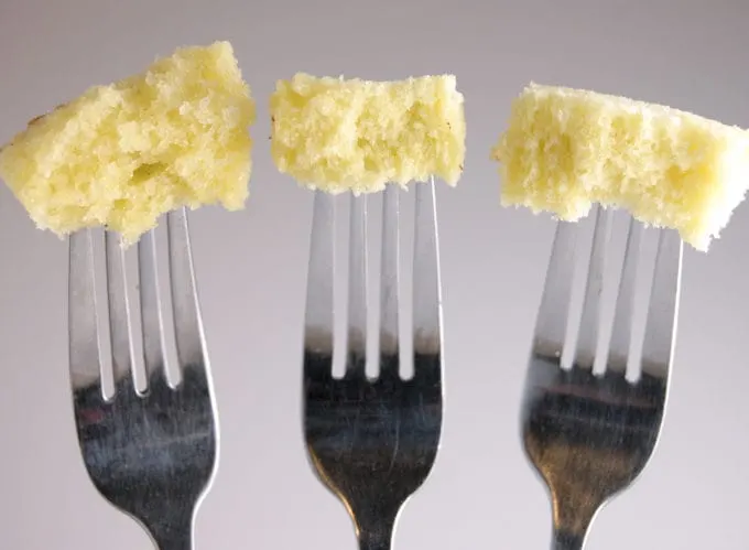 Closeup of three forks with a bite of cake at the end of each fork. Gray background