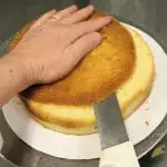 a pair of hand slicing off the top of a cake with a long knife