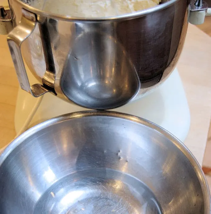 A stand mixer bowl full of buttercream with a smaller bowl of warm water underneath