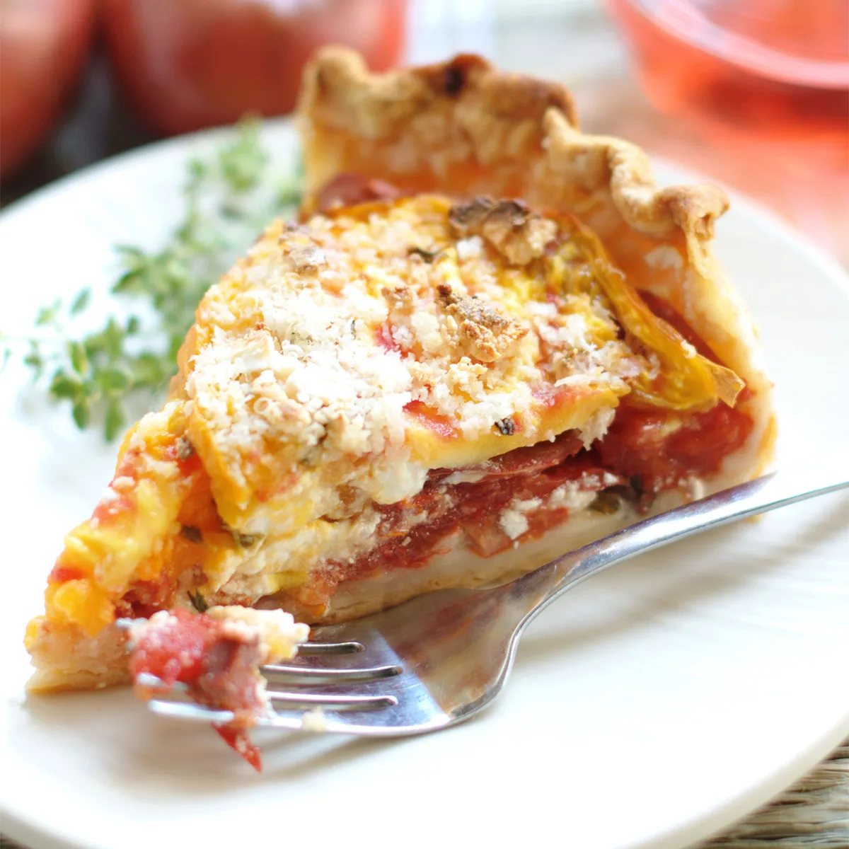 a slice of heirloom tomato pie on a white plate with a fork.