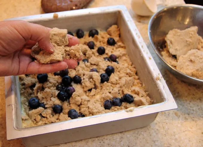 a hand sprinkling crumb topping onto a cake