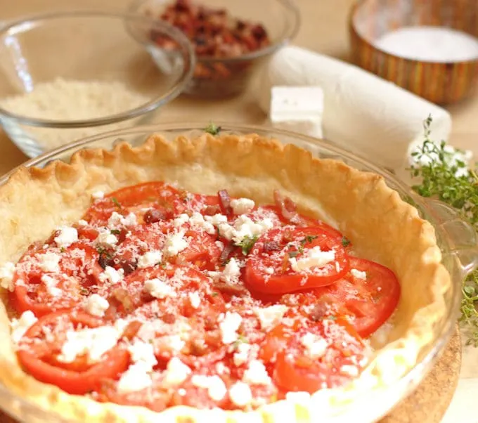 a pie shell filled with heirloom tomatoes and cheese ready for more layering