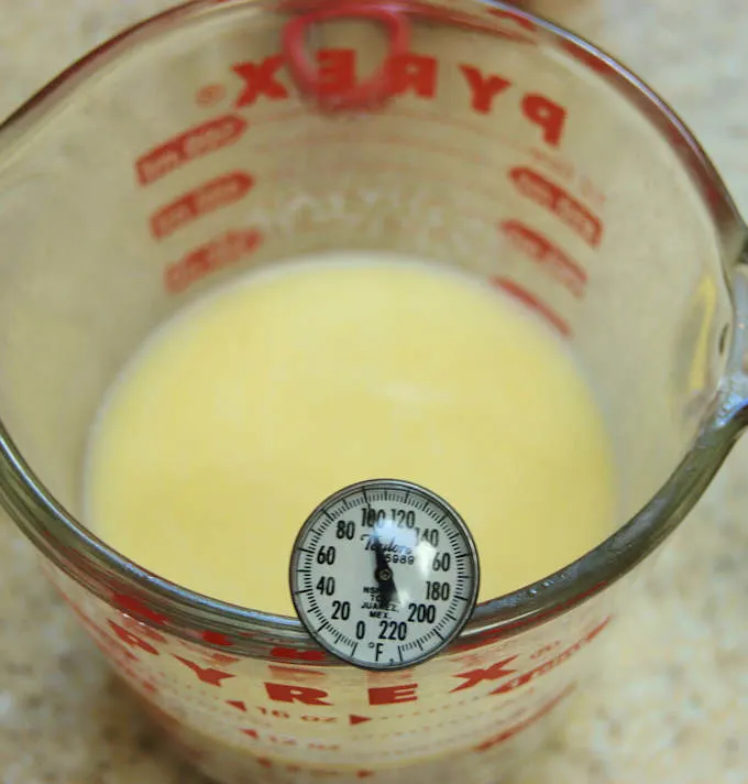 a measuring cup with milk and thermometer reads 100 degrees