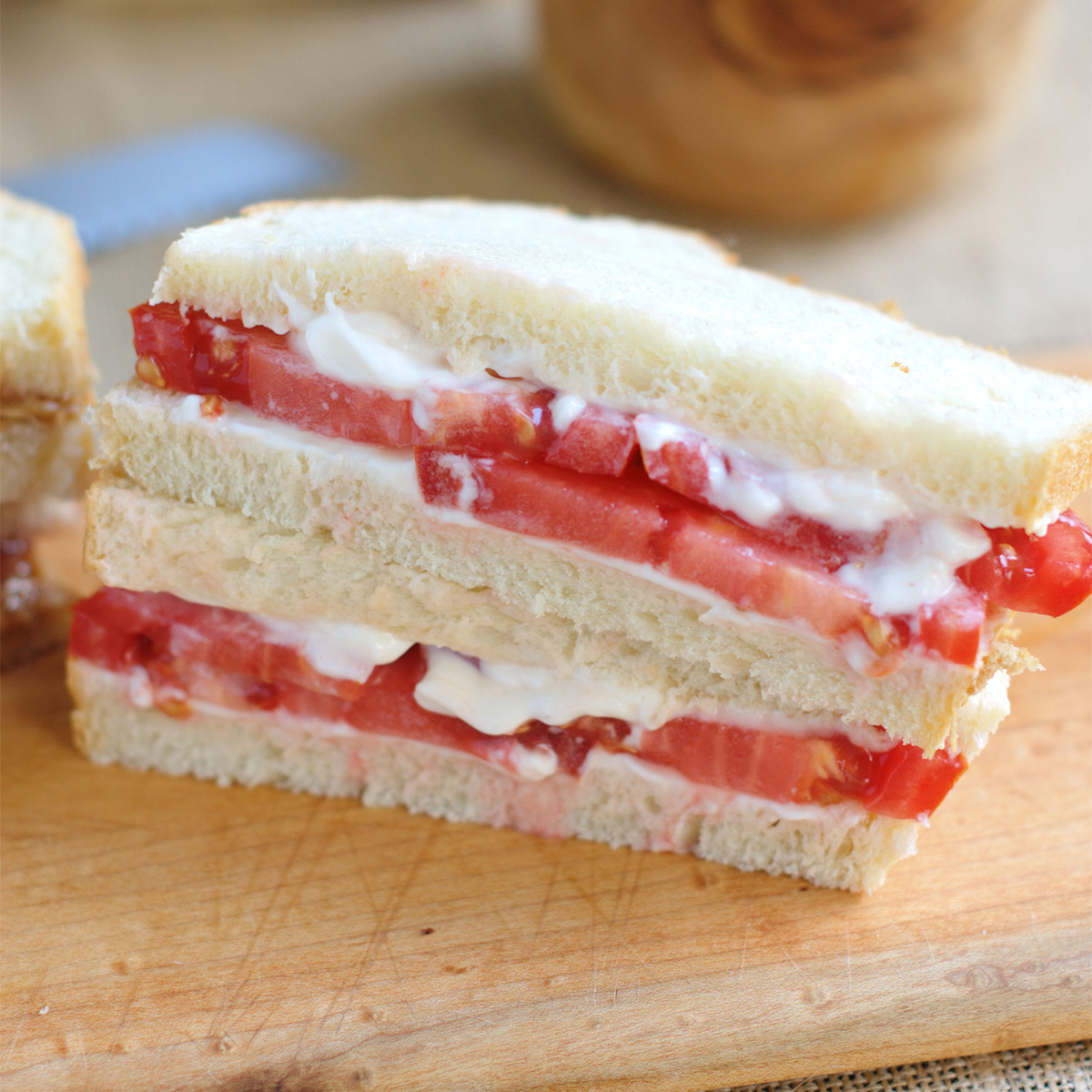 a white bread tomato sandwich on a cutting board.