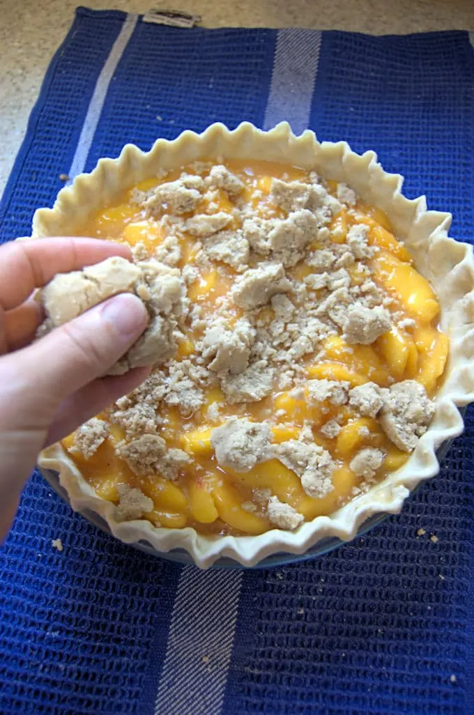A hand crumbling topping on a peach pie.
