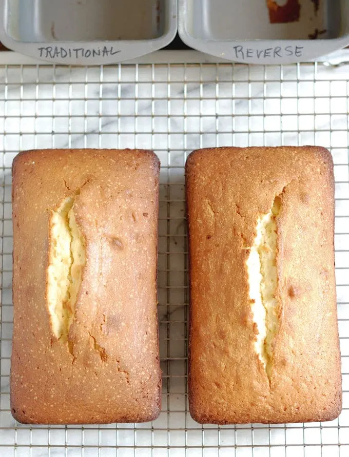 Two pound cakes on a cooling rack with cake pans in the background.