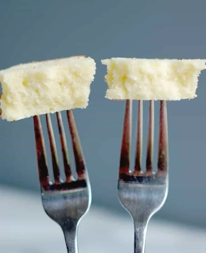 Two forks each with a bite of cake at the end against a gray background