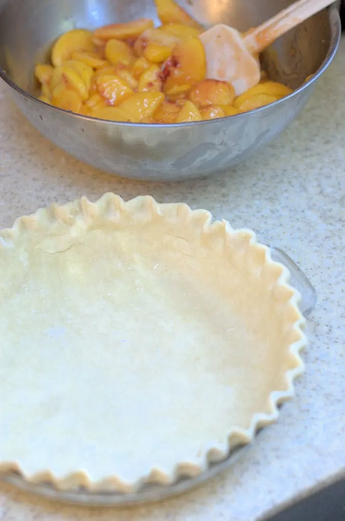 peach pie filling in a bowl next to an unbaked and a pie shell.