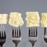 Four forks each with a bite of cake at the end. Gray background.