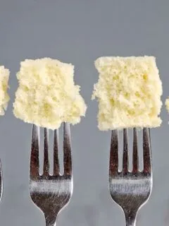 Four forks with pieces of cake at the end of each fork. Gray background.