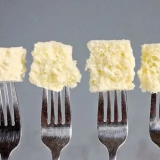 Four forks with pieces of cake at the end of each fork. Gray background.