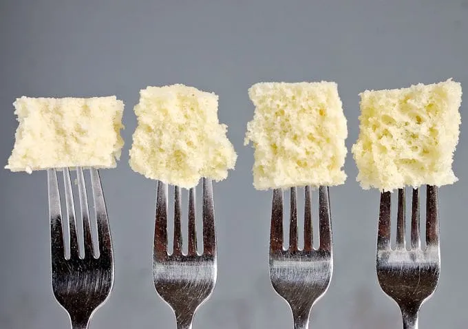 Four forks with pieces of cake at the end of each fork. Gray background.