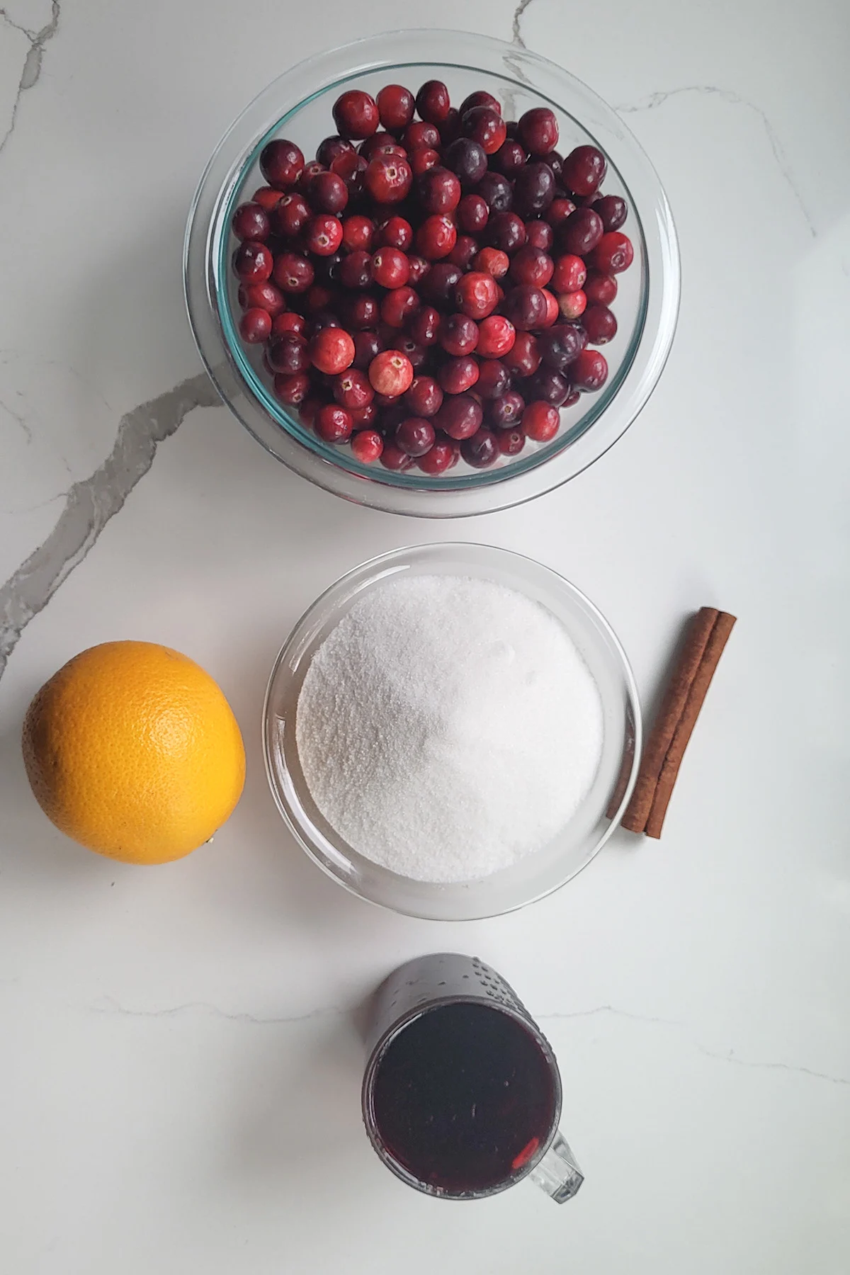 ingredients for cranberry compote in glass bowls on a white surface.