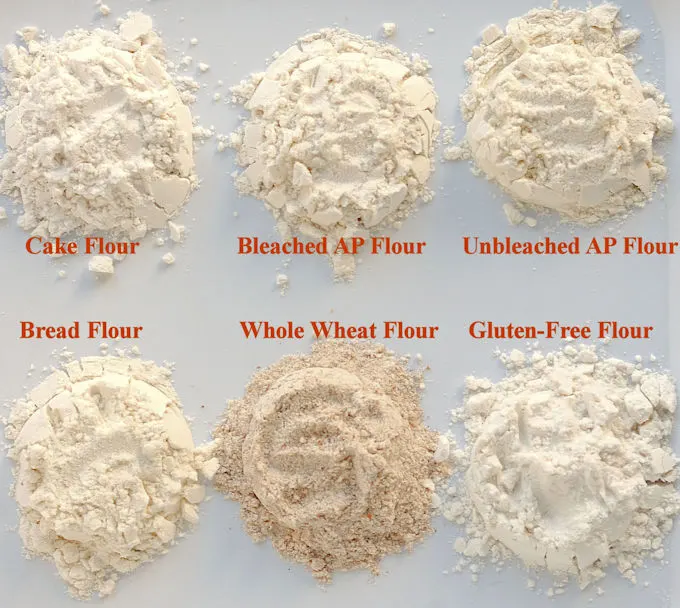 Piles of 6 different types of flour arranged on a white surface. Text overlay labels each flour.