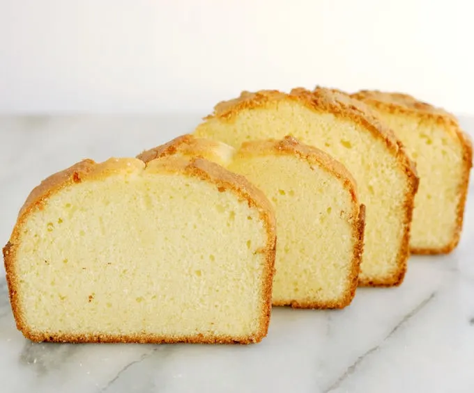 Four slices of pound cake standing in a row on a marble slab. cake batter sugar amounts.
