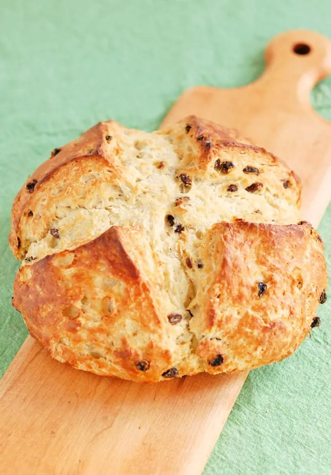 a loaf of Irish soda bread with raisins on a wooden board with a green background