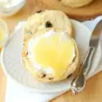 a raisin scone with clotted cream and lemon curd on a white plate