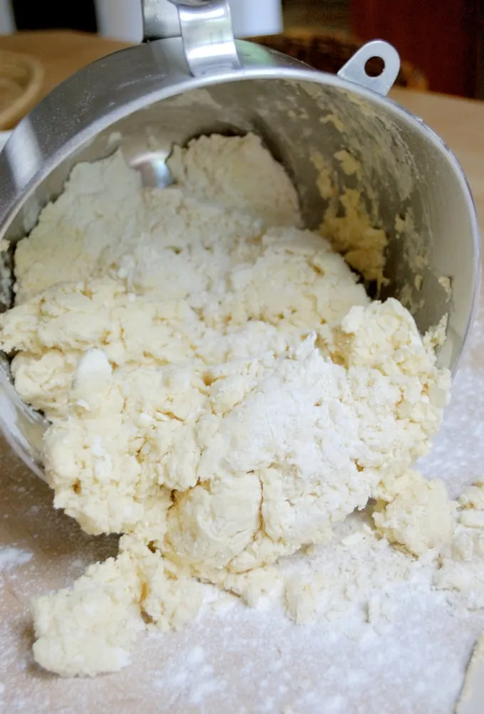 A mixer bowl with partially mixed dough being poured onto a table.