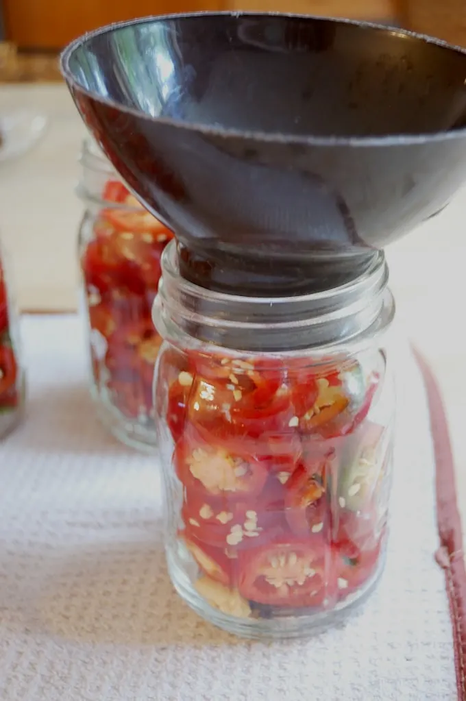 a canning funnel on a canning jar full of sliced jalapenos