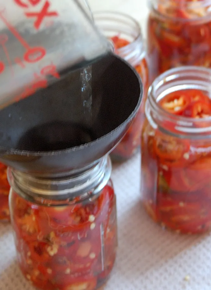 pouring bring over jalapeno peppers in canning jars.