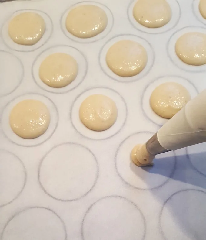 piping french macarons on a sheet pan