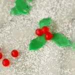 a closeup shot of marzipan holly & berries against a sugar covered surface