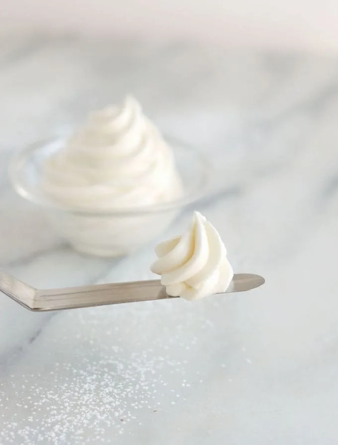 a swirl of cream cheese frosting on a small spatula with a bowl of icing in the background