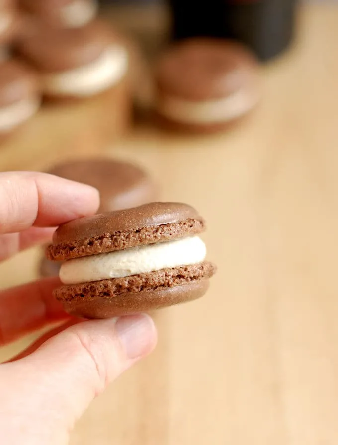 a hand holding a chocolate macaron with baileys irish cream filling