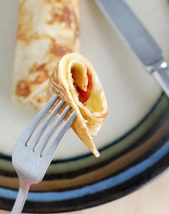 A bite of savory Dutch Pancake with speck and Gouda cheese on the end of a fork