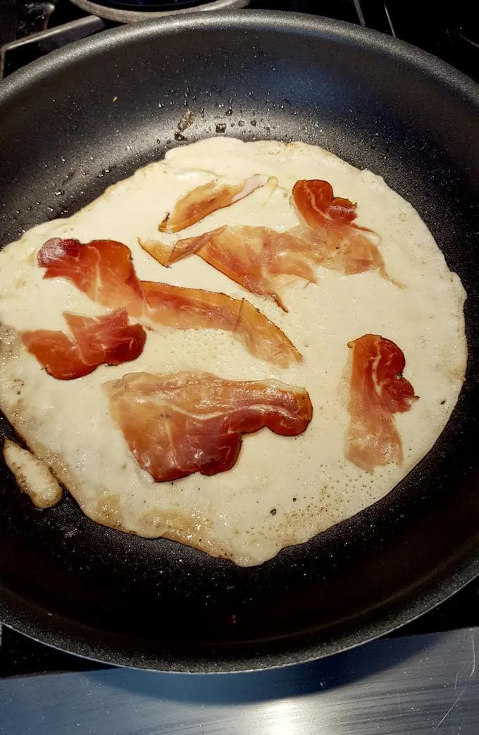 a pancake in a pan with pieces of bacon on top