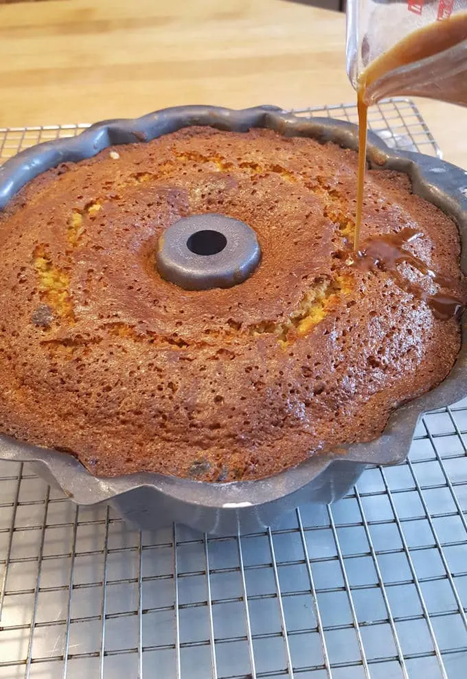 a bundt cake on a cooling rack with syrup being poured over the top