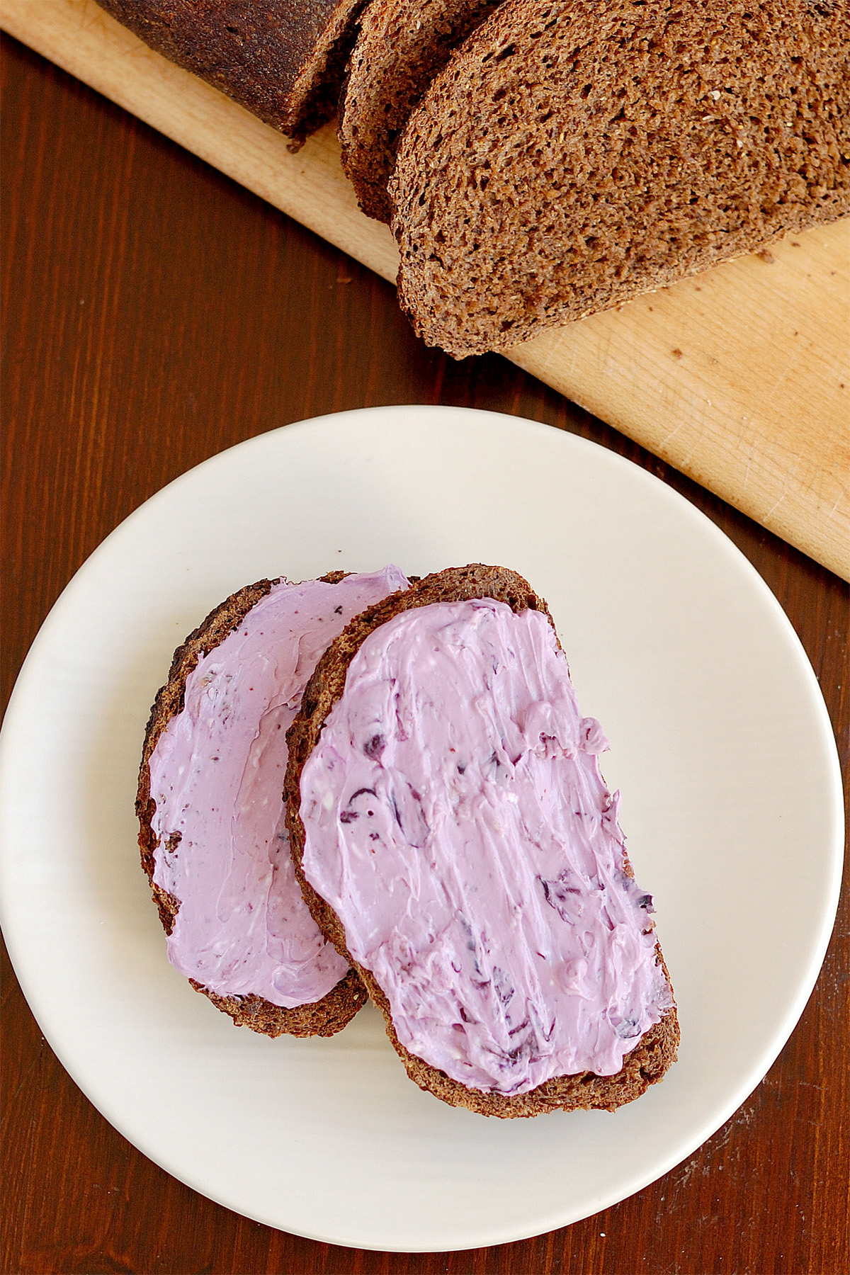 two slices of pumpernickel bread with blueberry cream cheese topping on a white plate.
