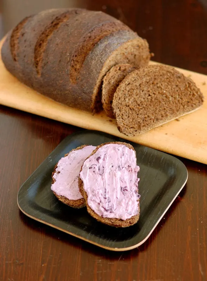 two slices of pumpernickel rye bread with blueberry cream cheese in foreground, loaf in background