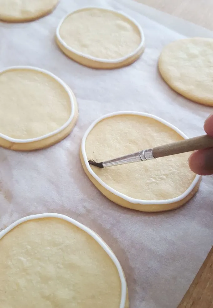 brushing royal icing on a sugar cookie