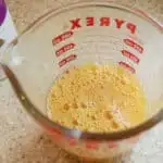 A glass measuring cup with whisked eggs on a marble surface.