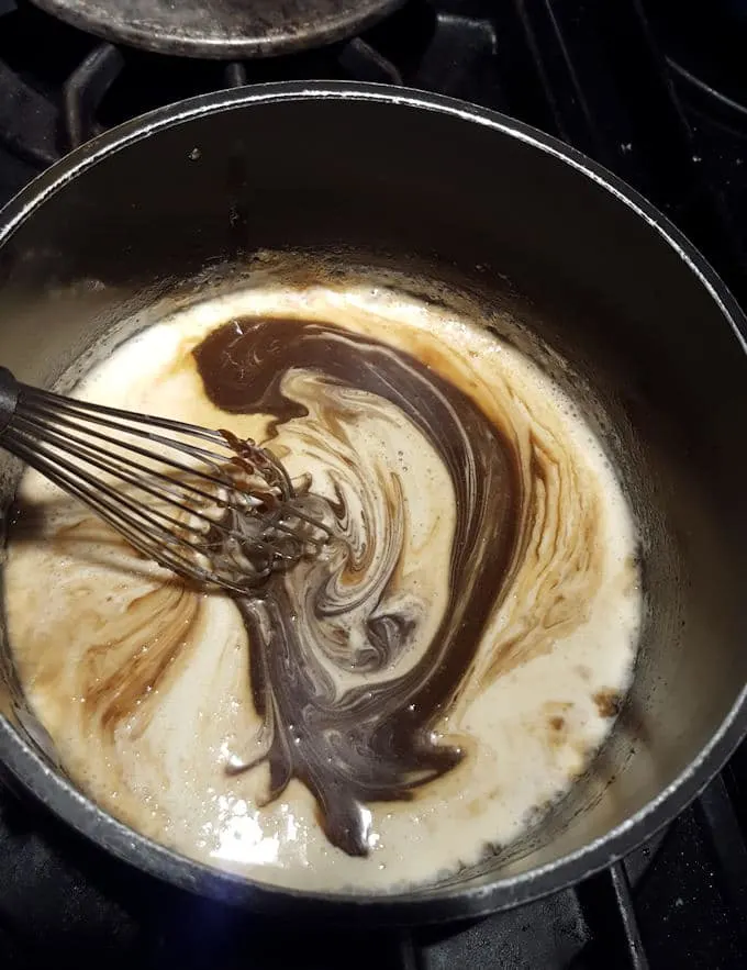 photos shows a pot with a whisk adding cream into butterscotch sauce