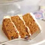 a slice of carrot cake with cream cheese frosting on a white plate with a fork