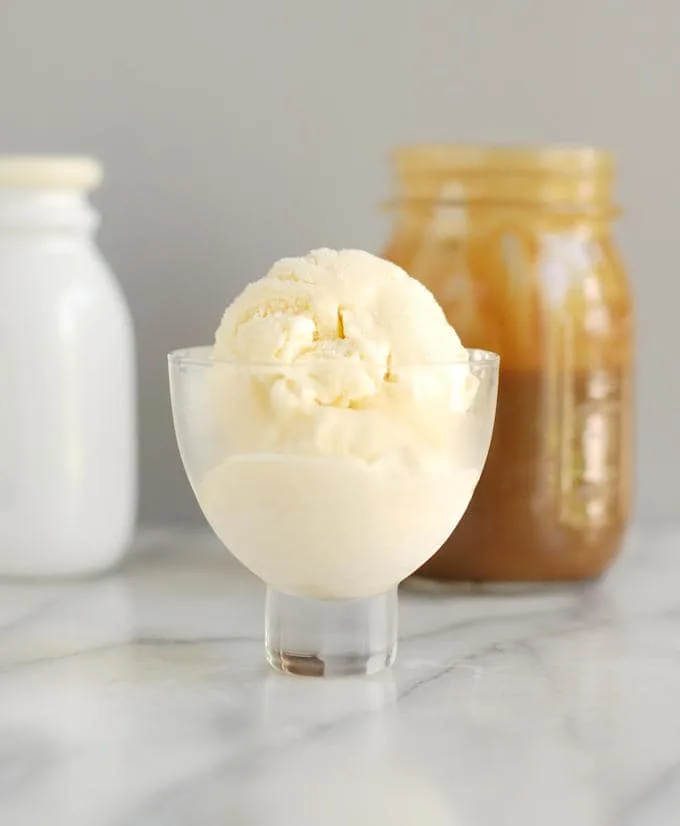 a glass bowl filled with creme fraiche ice cream with a jar of butterscotch sauce in the background.