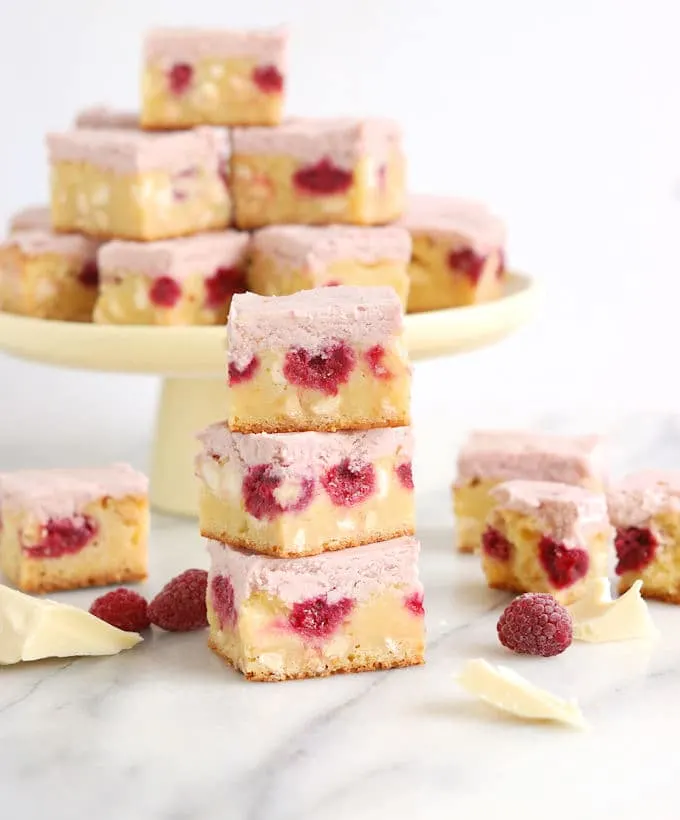 a stack of white chocolate brownies with raspberries on a marble surface
