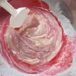 a spatula mixing raspberry puree into a bowl of white chocolate