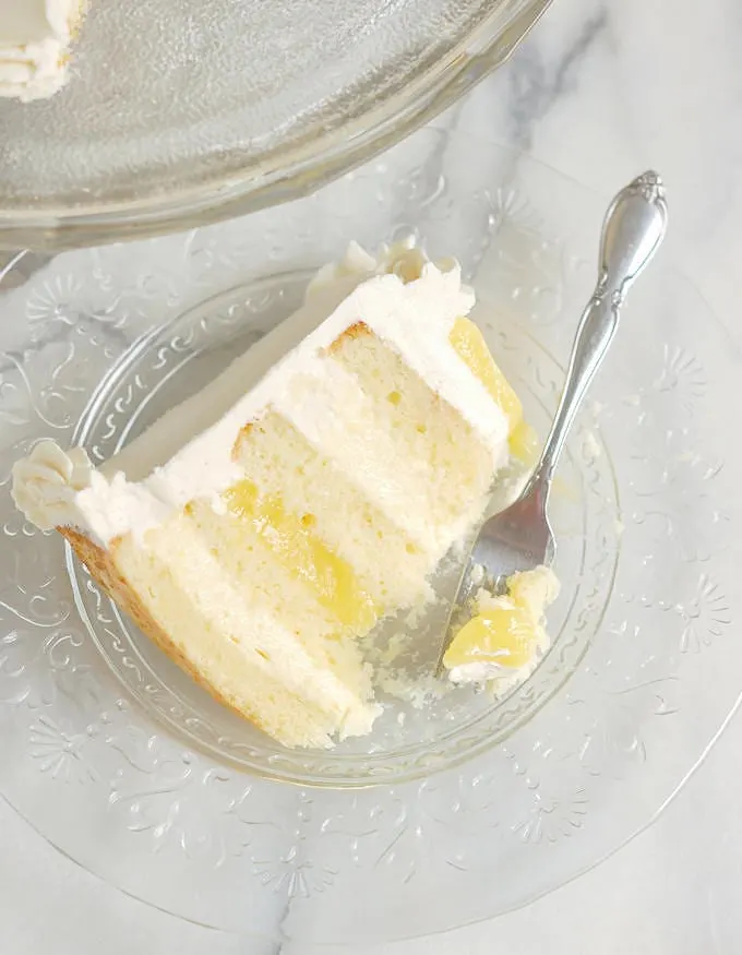 a partially eaten slice of lemon mousse layer cake on a glass plate with a fork