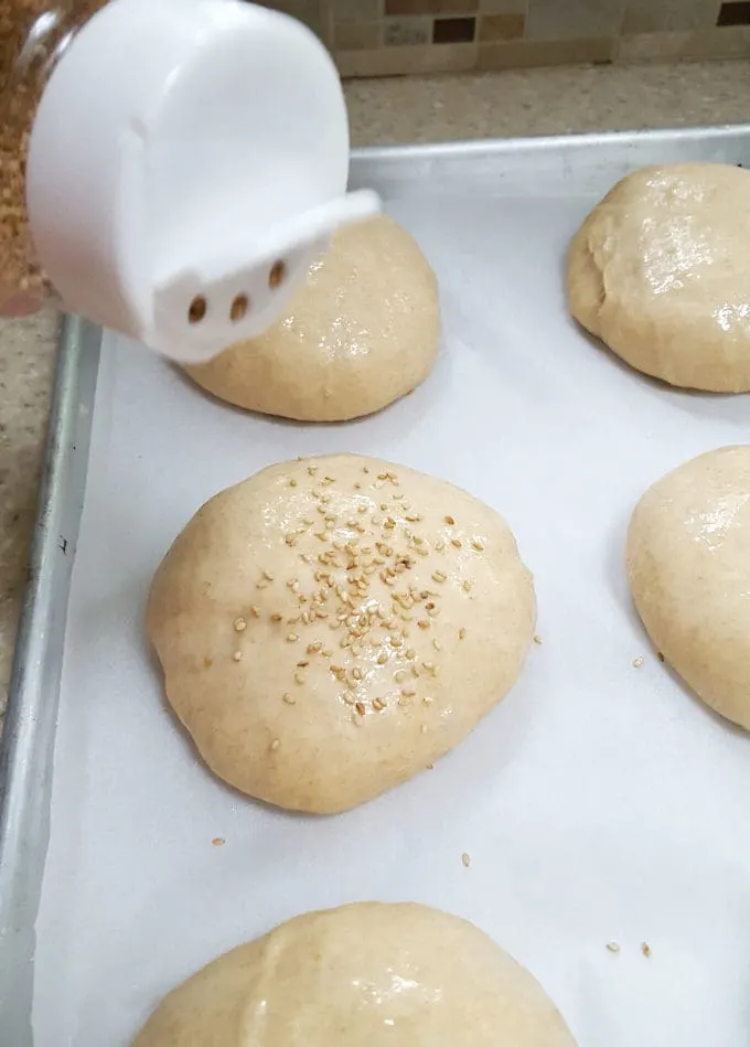 sprinkling sesame seeds on whole wheat burger buns