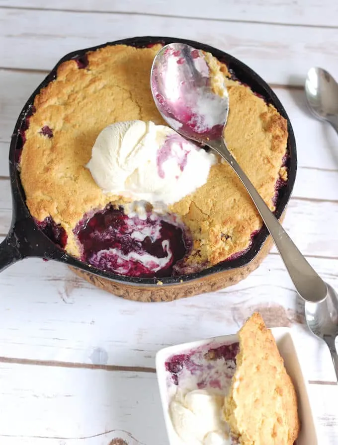 a skillet with blueberry cobbler and vanilla ice cream with a serving spoon