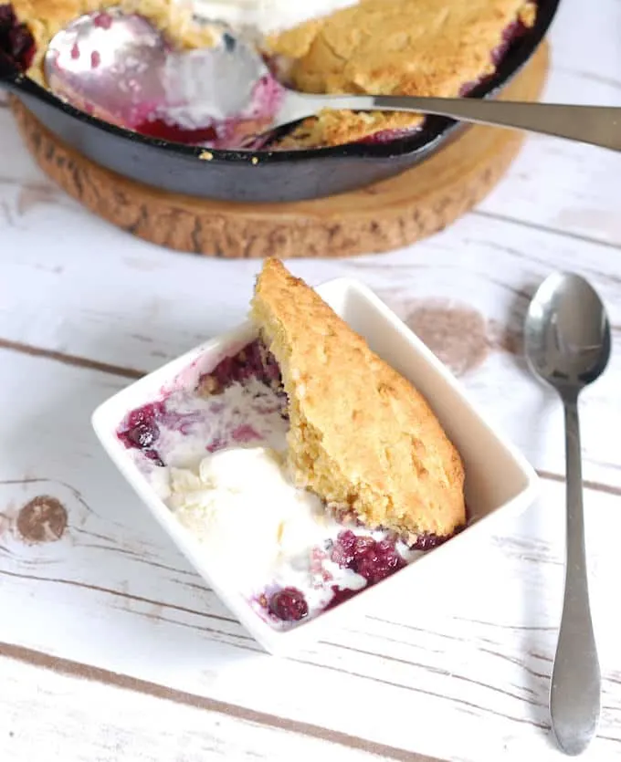 a bowl of blueberry cornbread cobbler with vanilla ice cream