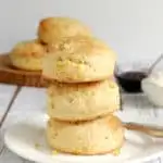 a stack of 3 sweet corn scones on a white plate with jam and cream in the background