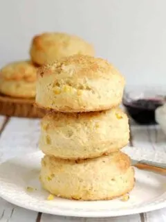 a stack of 3 sweet corn scones on a white plate with jam and cream in the background