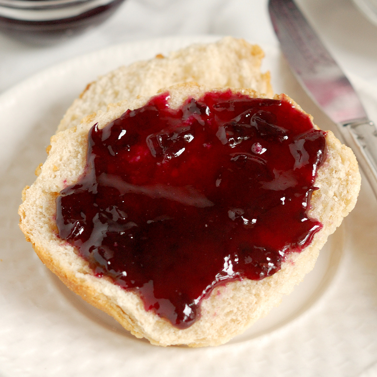 a piece of bread on a white plate with concord grape jam on top,