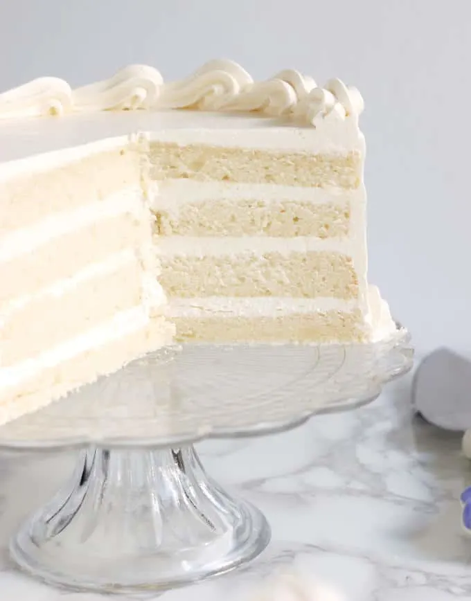 An cross section of a four layer velvety soft white cake 1/2 on a glass cake stand.